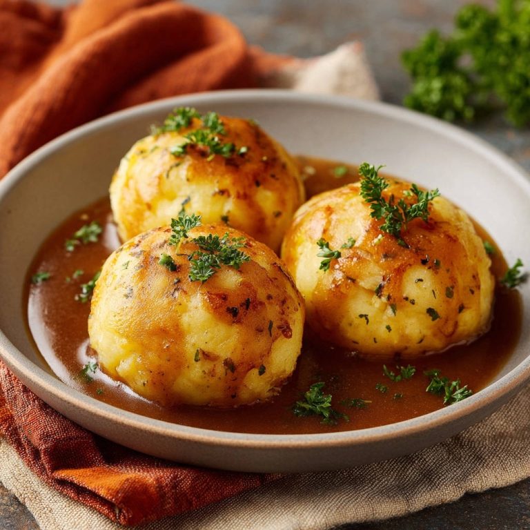 Herzhafte Kartoffelknödel mit Bratensoße serviert in einer tiefen Schüssel, garniert mit frischer Petersilie. Die Knödel sind von goldbrauner Farbe.