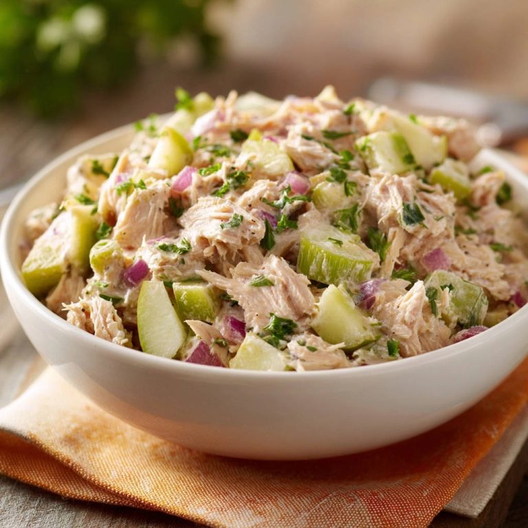 Aromatischer Hähnchensalat mit Apfel und Rotzwiebel in Nahaufnahme, angerichtet in einer weißen Schüssel auf einem rustikalen Untergrund.