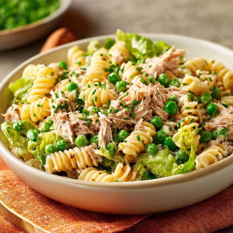 Cremiger Thunfisch-Nudelsalat, serviert in einer Schüssel. Eine Nahaufnahme zeigt die cremige Konsistenz mit Erbsen und frischen Kräutern.