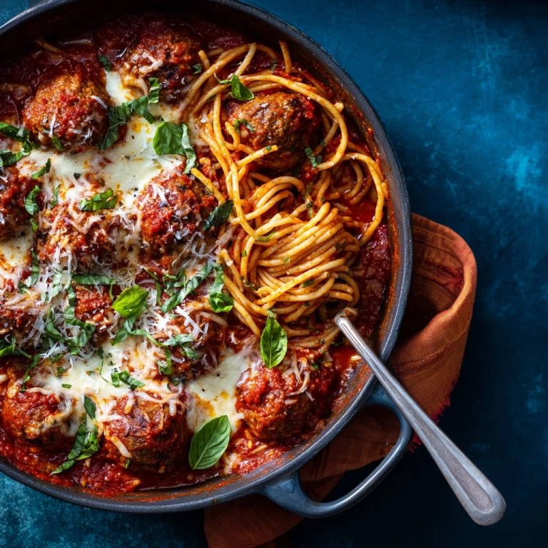 Pfannen-Spaghetti mit saftigen Hackbällchen und Käse, von oben fotografiert, mit frischem Basilikum garniert und mit Käse bedeckt.