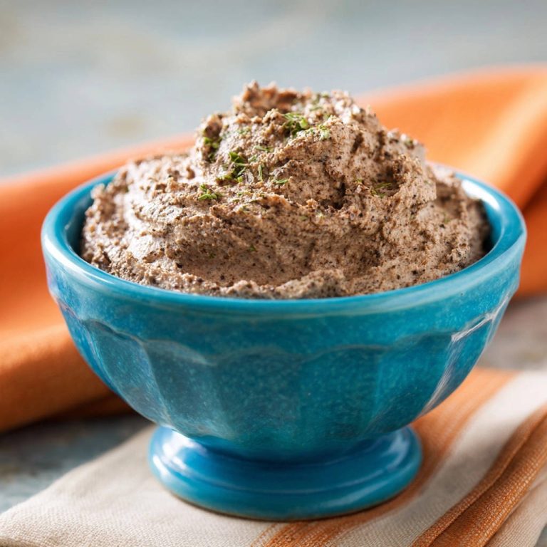 Pilz-Pâté in einer blauen Schüssel serviert, mit frischen Kräutern garniert und eine unwiderstehlich cremige Textur aufweisend.