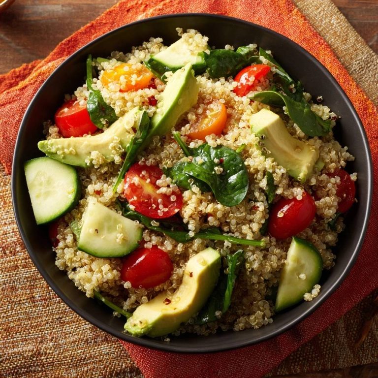 Frischer Quinoa-Avocado-Salat in einer dunklen Schüssel, von oben betrachtet, mit Avocado, Tomaten und Gurke angerichtet.