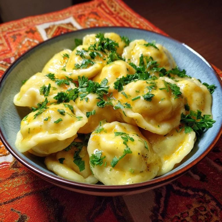 Kürbis-Pelmeni, serviert in einer Schüssel, garniert mit frischen Kräutern, präsentiert ein appetitliches Gericht. Der Blick von oben zeigt die leckeren Teigtaschen.