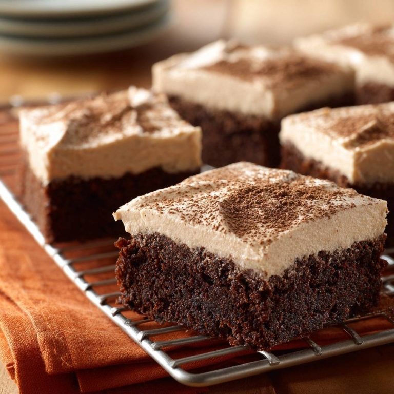 Saftige Schoko-Brownies mit Cremefrosting in Nahaufnahme auf einem Kuchengitter, bestreut mit Kakaopulver, perfekt zum Genießen.