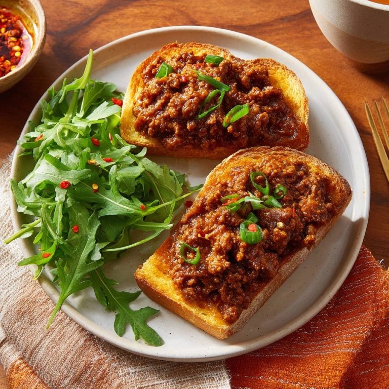 Würziges Hackfleisch-Toast serviert auf einem Teller mit frischem Rucola-Salat und Chiliöl für ein köstliches Mittagessen.