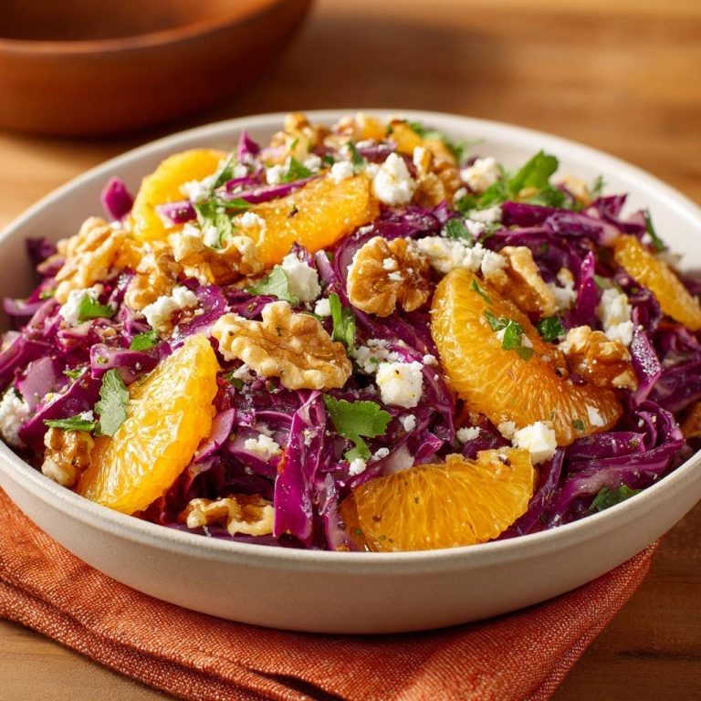 Frischer Rotkohl-Orangen-Salat mit Walnüssen und Feta in einer Schüssel, serviert in einer Nahaufnahme von oben. Der farbenfrohe Salat ist mit Walnüssen und Feta garniert.