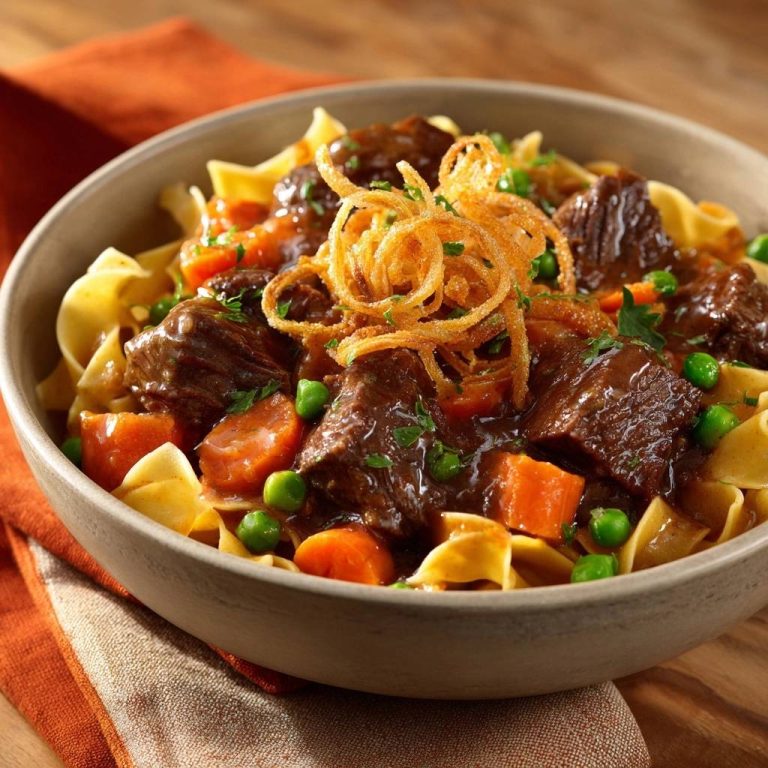 Rindergulasch mit Bandnudeln, serviert in einer Schüssel, garniert mit knusprigen Zwiebelringen und frischer Petersilie. Ein herzhaftes Gericht zum Genießen.