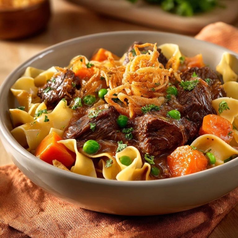 Zartes Rindergulasch mit Nudeln, serviert in einer Schüssel, garniert mit knusprigen Zwiebeln und Petersilie. Das herzhafte Gericht ist perfekt für ein gemütliches Abendessen.