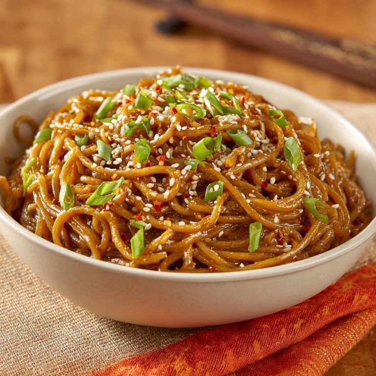 Glänzende Sesam-Chili-Nudeln, garniert mit frischen Frühlingszwiebeln, Sesam und Chiliflocken, serviert in einer cremefarbenen Schüssel.