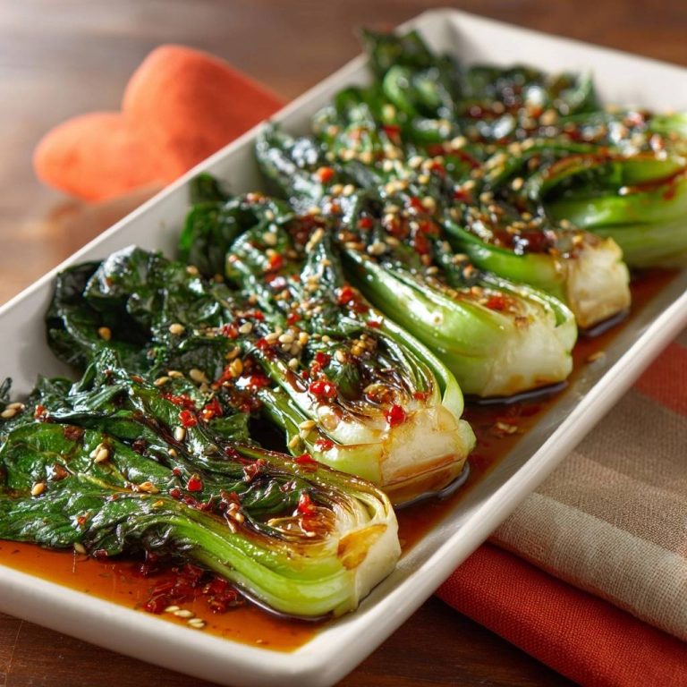 Knackiger Pak Choi mit Sesam-Chili-Sauce serviert auf einem weißen Teller, garniert mit Chili-Flocken und Sesam. Eine Nahaufnahme des aromatischen Gerichts.