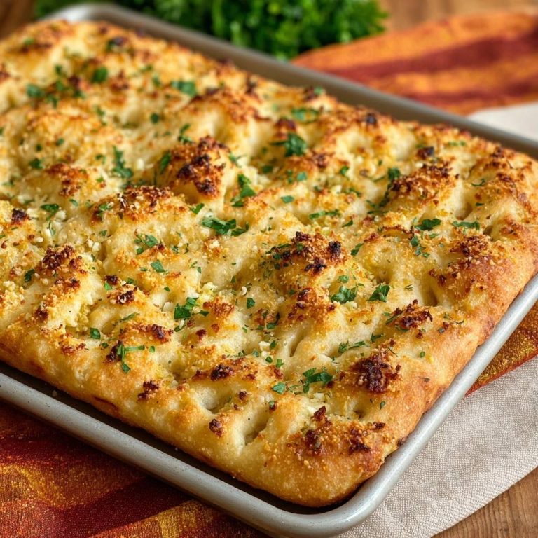 Knusprige Parmesan-Focaccia in einer Backform, serviert in einer Draufsicht, mit goldener Kruste und frischen Kräutern garniert.