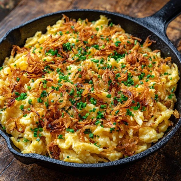 Pfannige Käsespätzle mit knusprigen Zwiebeln, serviert in einer gusseisernen Pfanne, garniert mit frischen Kräutern und knusprigen Zwiebeln.