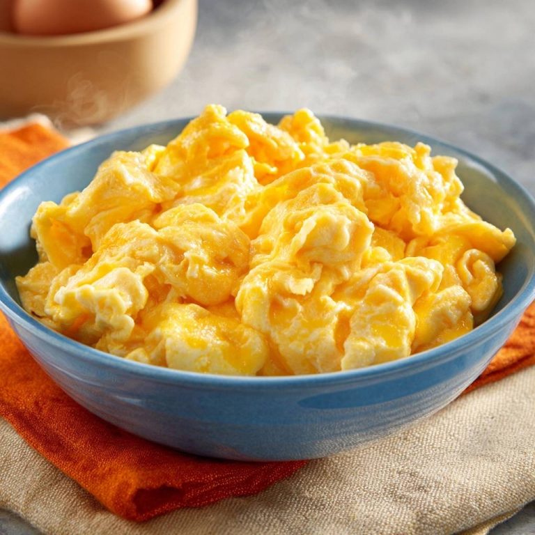 Cremiges fluffiges Rührei in einer blauen Schüssel, Nahaufnahme mit cremiger Textur und Dampf. Wunderbar zubereitetes Frühstück.