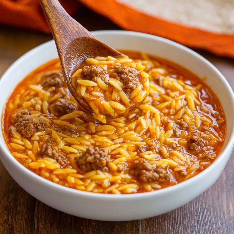 Ein-Topf-Orzo mit saftigem Hackfleisch zeigt eine Nahaufnahme, die mit einem Holzlöffel aus der Schüssel gehoben wird. Die köstliche Suppe ist frisch zubereitet.