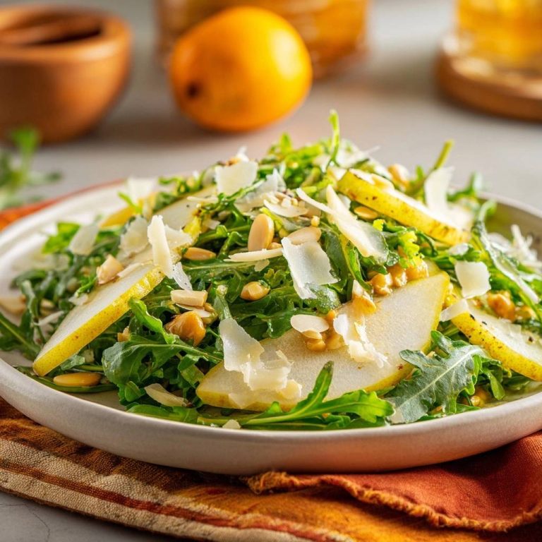 Frischer Rucola-Birnen-Salat serviert auf einem weißen Teller, garniert mit Mandelsplittern und Parmesan. Ein köstlicher und aromatischer Salat, perfekt für jede Gelegenheit.