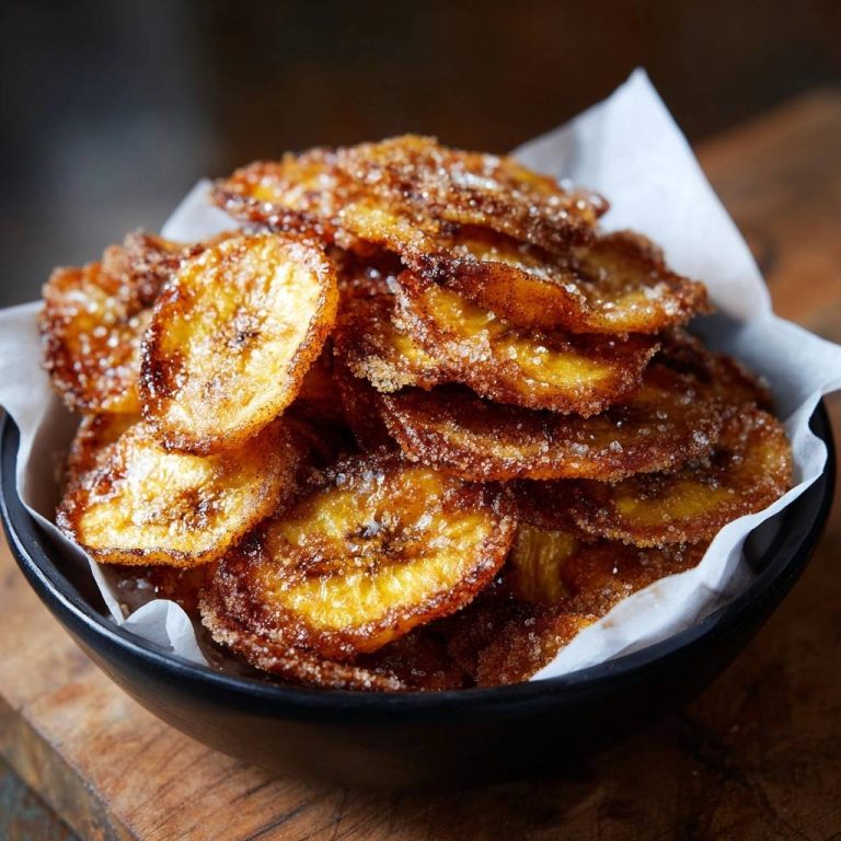 Knusprige Karamell-Bananen in einer schwarzen Schüssel, nah aufgenommen. Die frittierten Bananenscheiben sind reichlich mit Zucker bestreut.