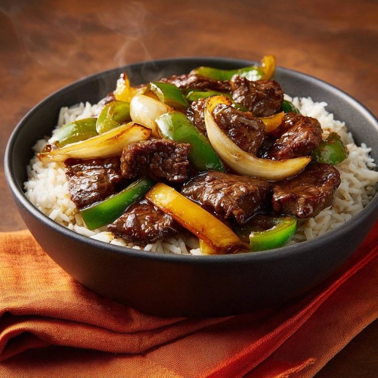 Rindfleisch-Paprika-Pfanne auf Reis in Nahaufnahme, dampfend heiß serviert in einer dunklen Schüssel, angerichtet auf fluffigem Reis.