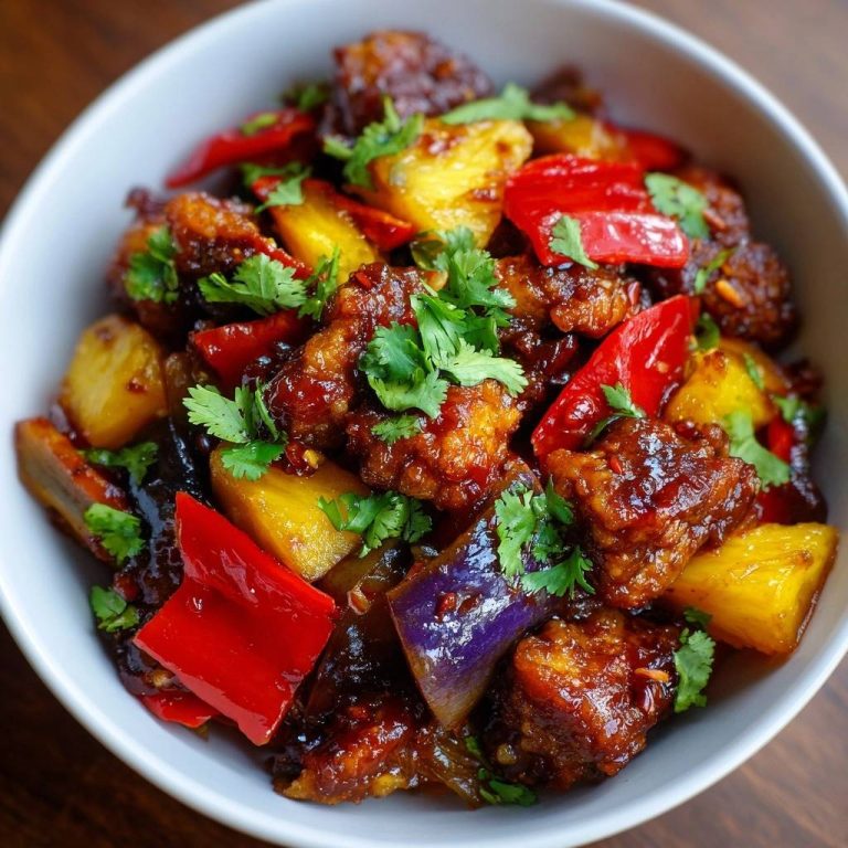 Knuspriges Süß-Sauer Hähnchen mit Ananas und Aubergine in einer Schüssel, von oben betrachtet mit frischer Petersilie garniert.