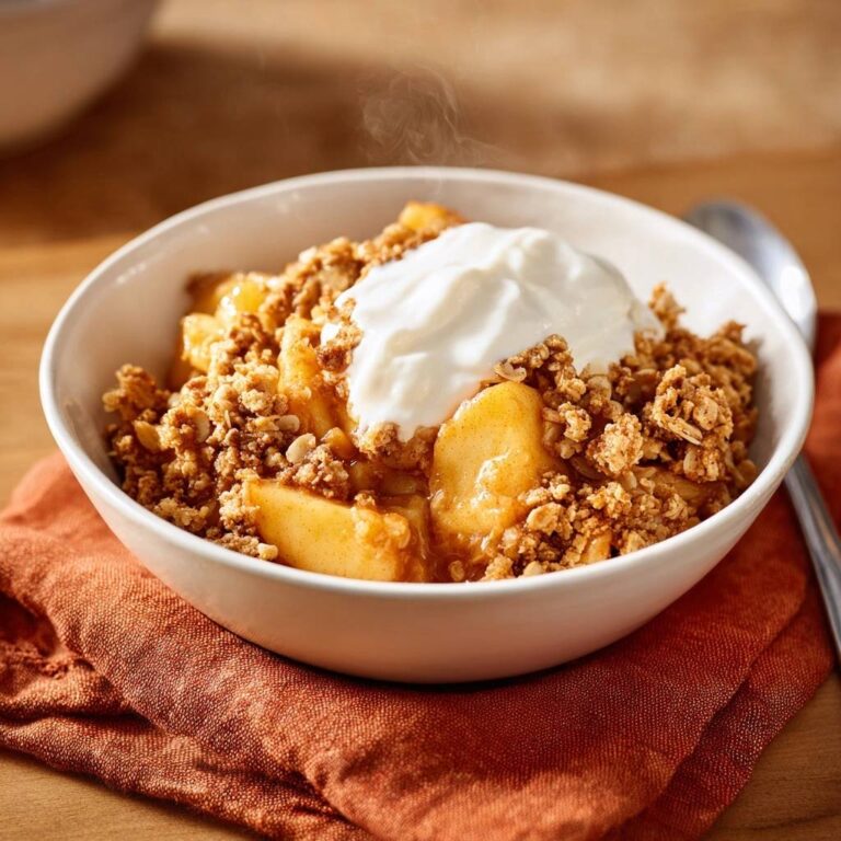 Warmer Apfel-Crumble mit Sahnehaube, serviert in einer weißen Schüssel, mit einem großzügigen Klecks Sahne als Topping.
